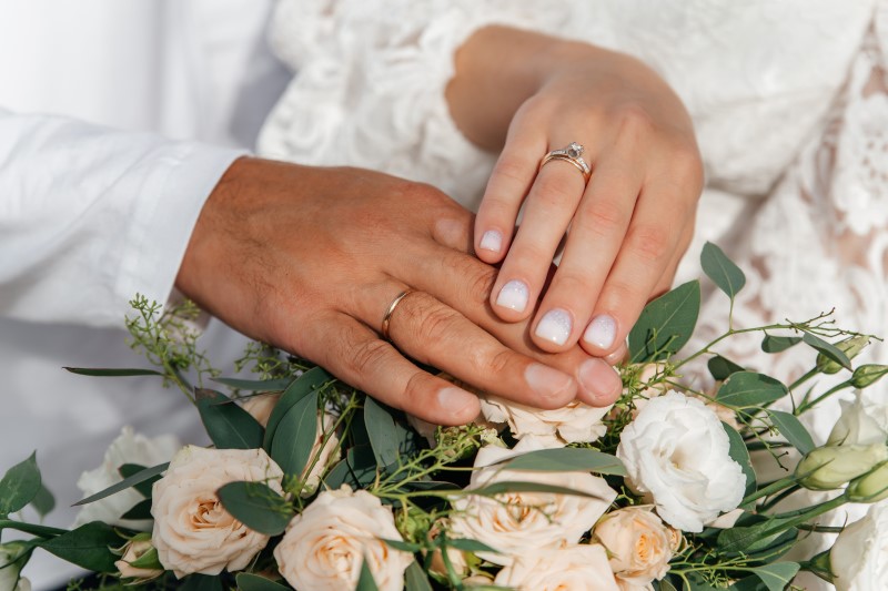 Hände von Braut und Bräutigam mit Ringen auf Hochzeitsblumenstrauß. Konzept der Ehe.
